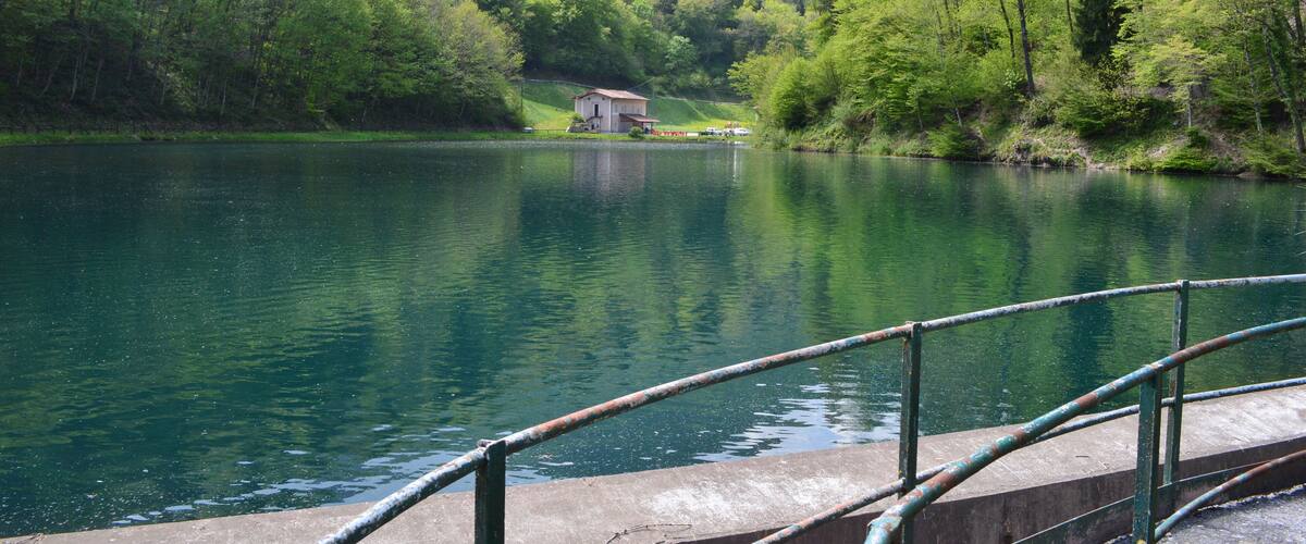 A calm lake surrounded by lush green hills and a small building on the shore.