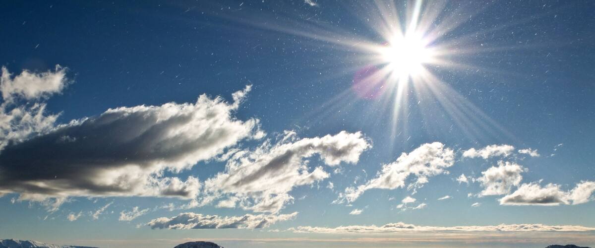 A snowy mountain landscape with a clear sky and the sun shining brightly.