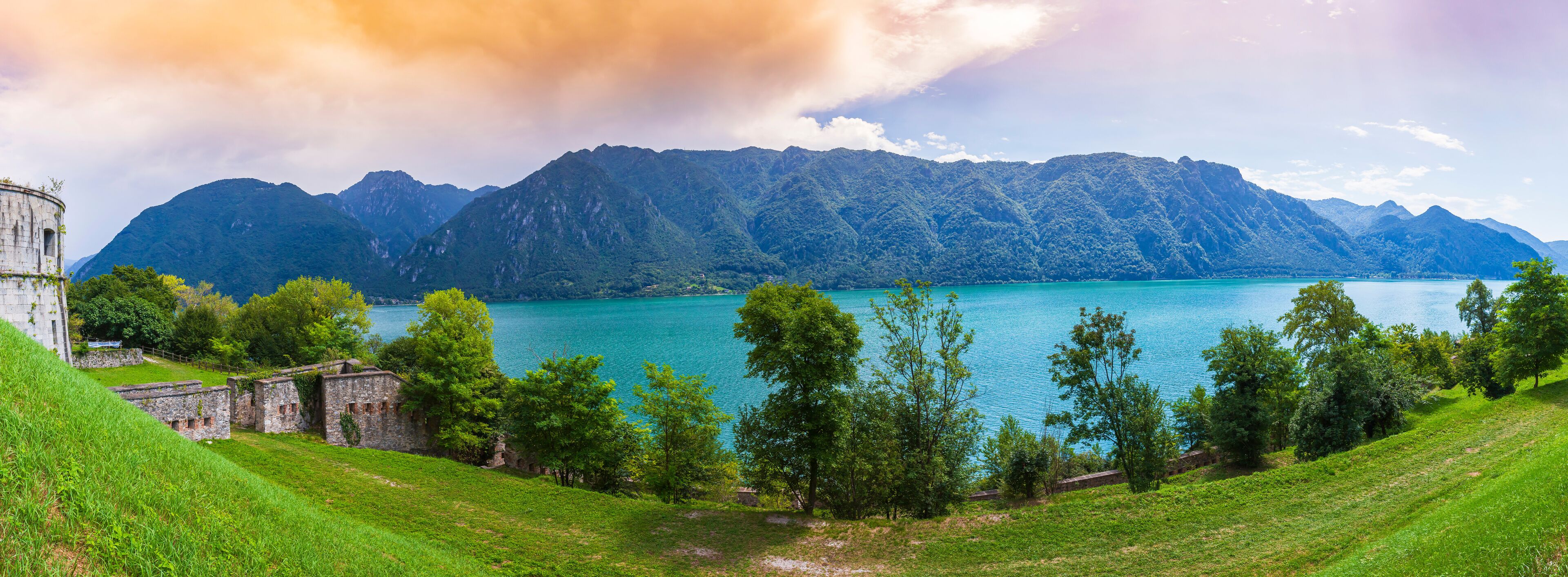 A mountainous landscape with a turquoise lake, green hills, and historical stone buildings.