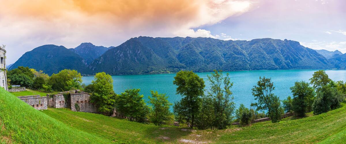 A mountainous landscape with a turquoise lake, green hills, and historical stone buildings.