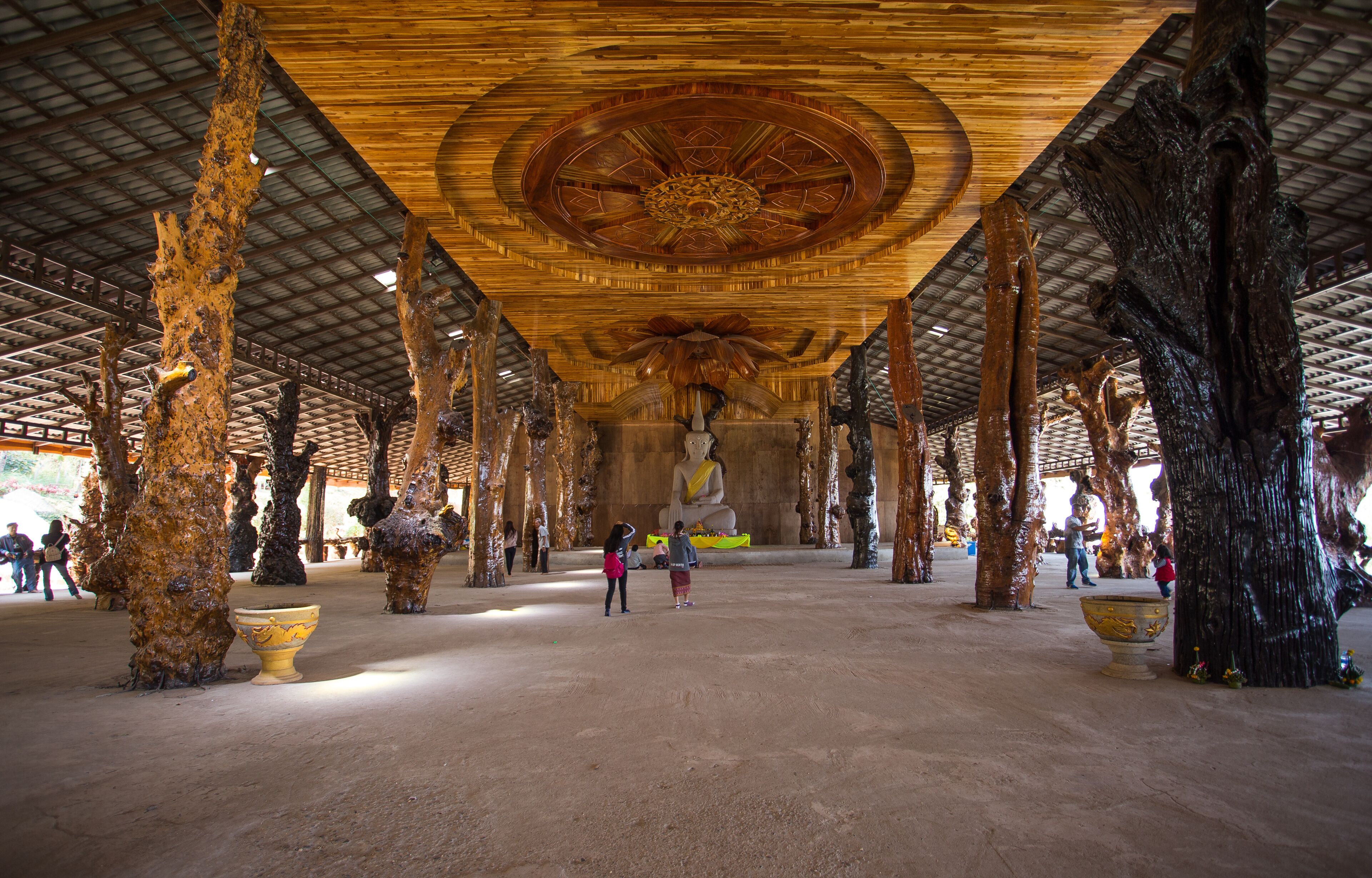A large indoor space with a high ceiling, featuring a central Buddha statue, wooden pillars, and large decorative urns.