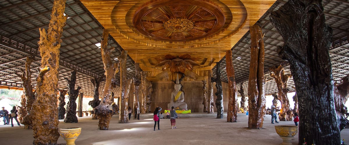 A large indoor space with a high ceiling, featuring a central Buddha statue, wooden pillars, and large decorative urns.