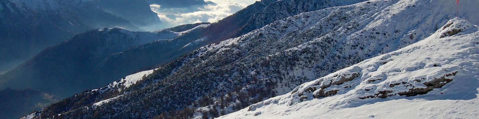 Paisaje montañoso cubierto de nieve, con cielo despejado y nubes distantes.