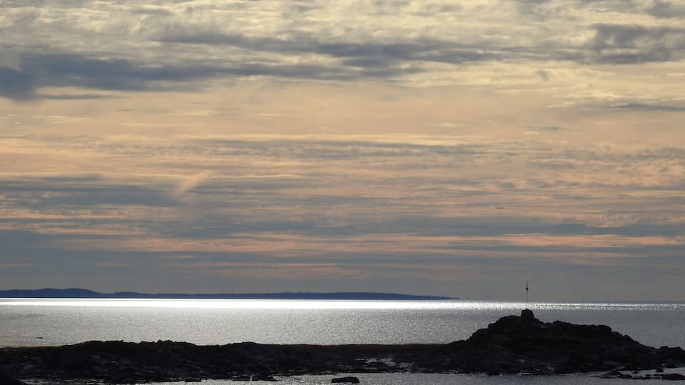 A rocky shoreline with scattered rocks in the water and a lighthouse in the distance.