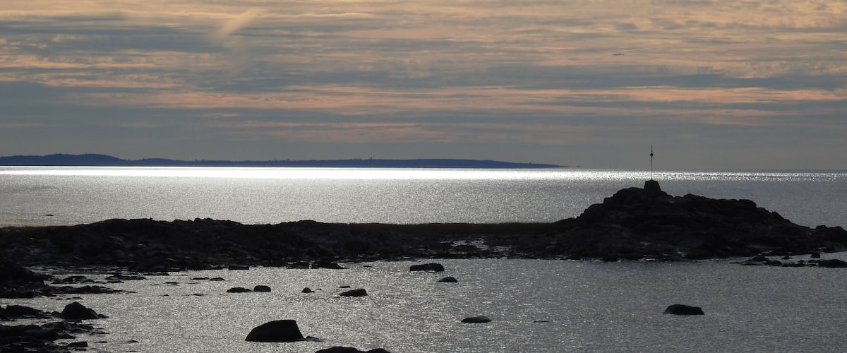 A rocky shoreline with scattered rocks in the water and a lighthouse in the distance.
