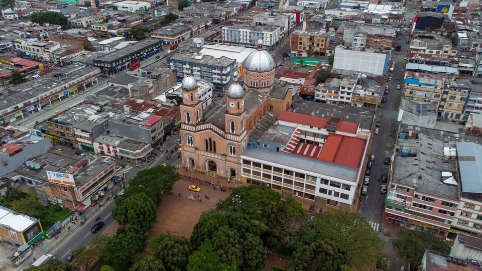 An aerial view of a city with a prominent church with two domes, surrounded by dense urban buildings and streets.