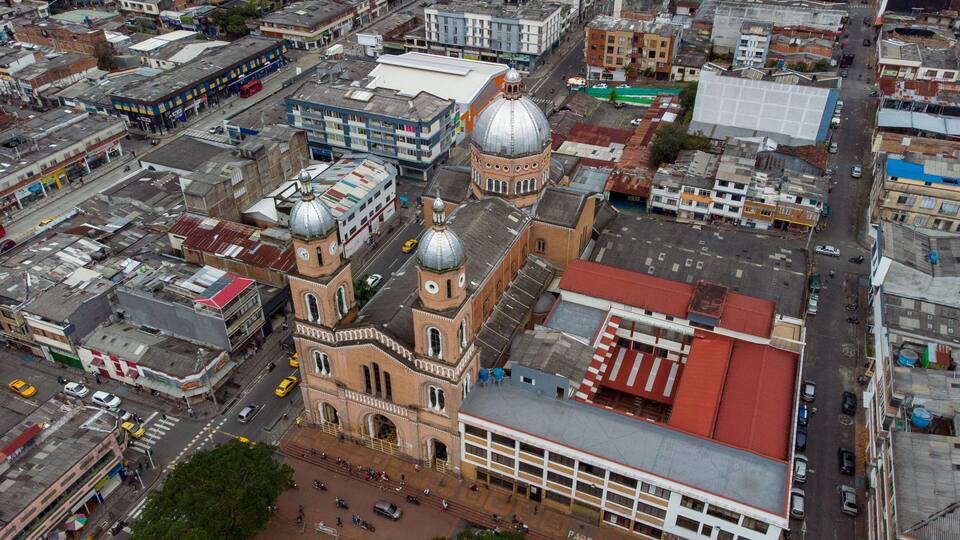 An aerial view of a city with a prominent church with a large dome and clock tower, surrounded by various buildings and streets.