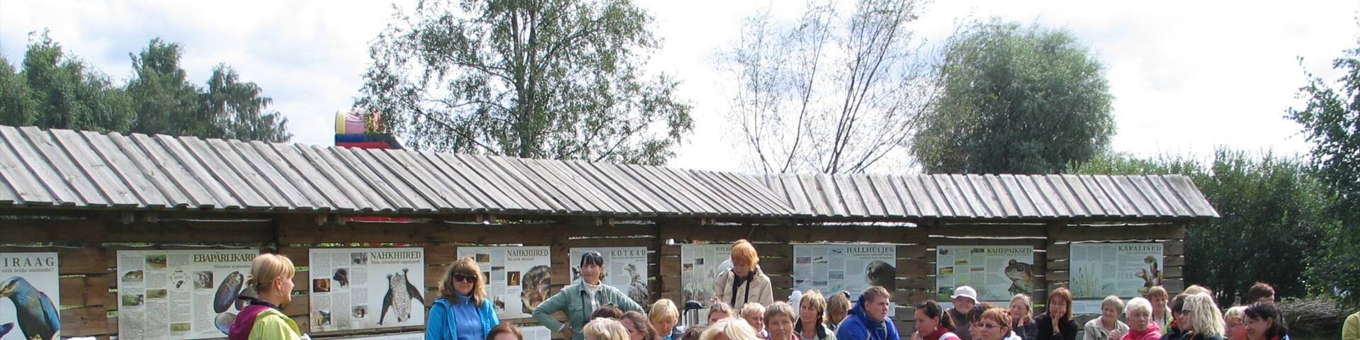 A group of people seated outdoors in a grassy area with a wooden structure in the background.