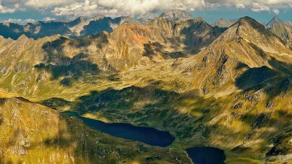 Eine Berglandschaft mit einem See und fernen Berggipfeln unter einem teils bewölkten Himmel.