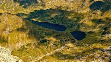 Un paisaje montañoso con un lago y cumbres distantes bajo un cielo parcialmente nublado.