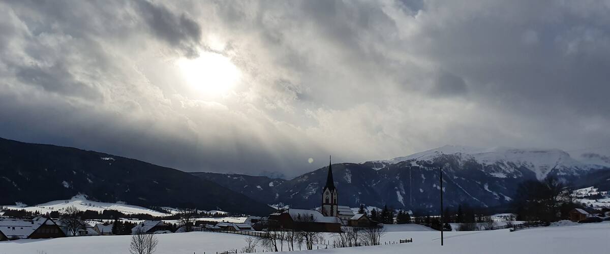A snow-covered village with a church and mountains in the background.