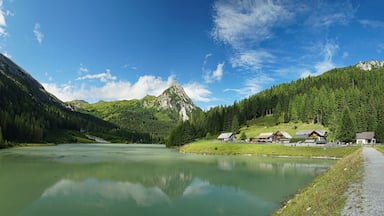 A mountain lake with reflections, surrounded by forested hills and houses.