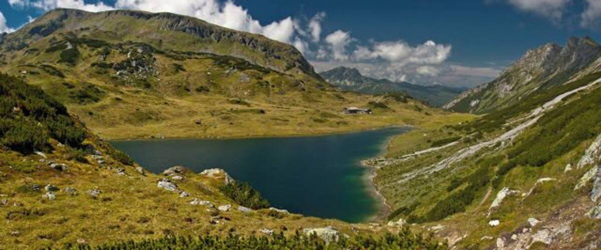 A mountain landscape with a lake, a clear sky, and a small cabin.
