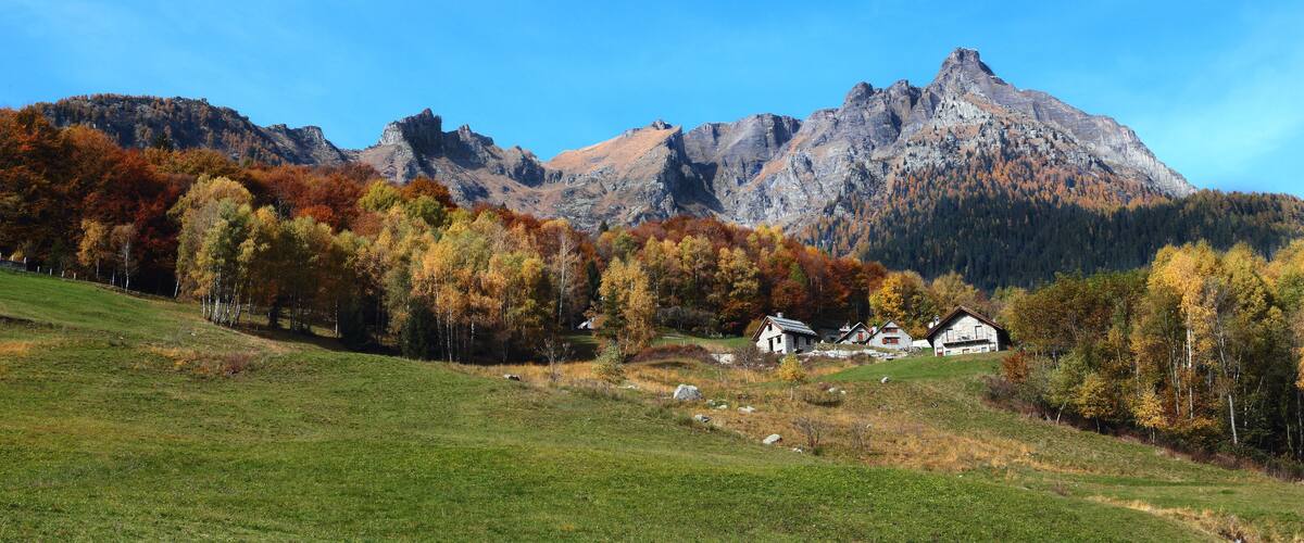 A mountainous landscape with autumn-colored trees and a few houses in the foreground.