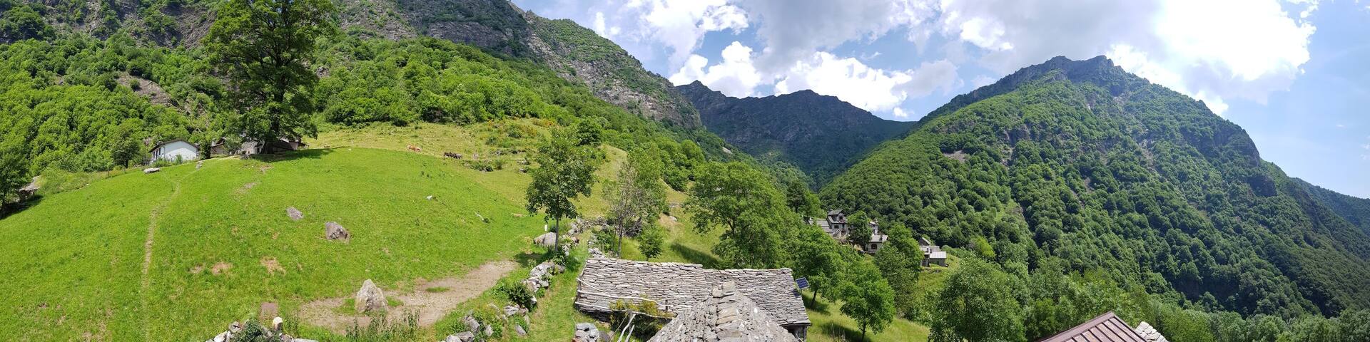 A mountainous landscape with green fields, a stone house, and a small building.