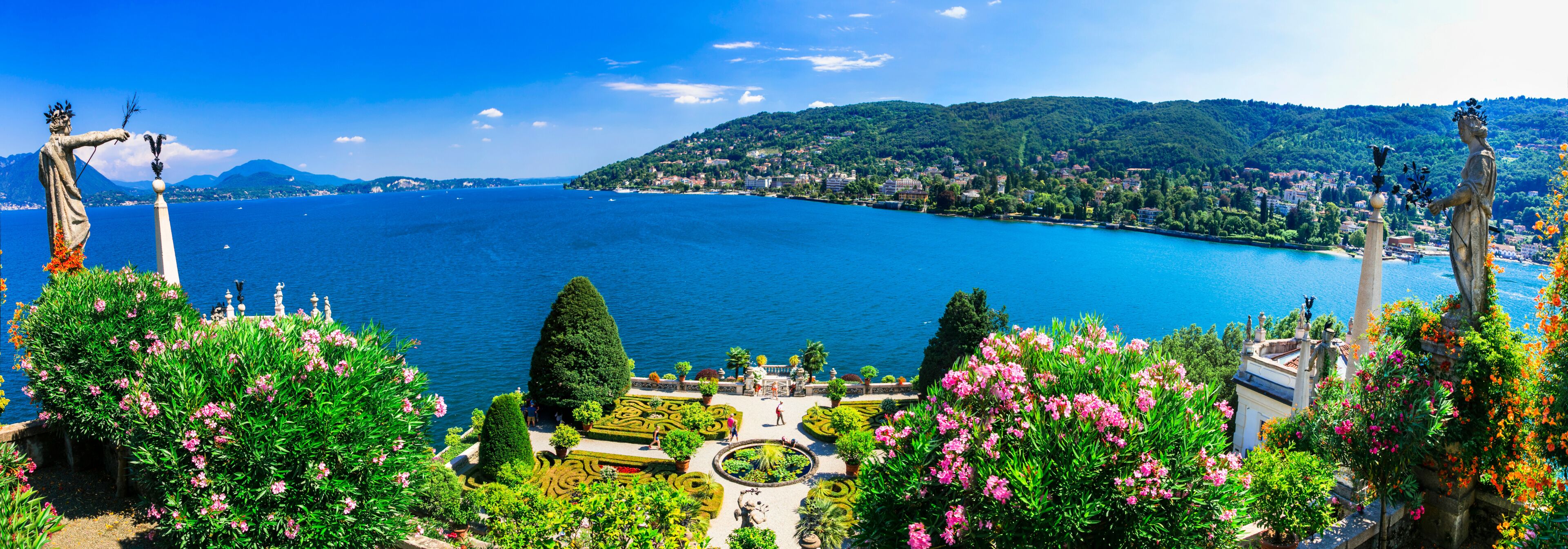 A coastal landscape with a large body of water, green hills, and statues.