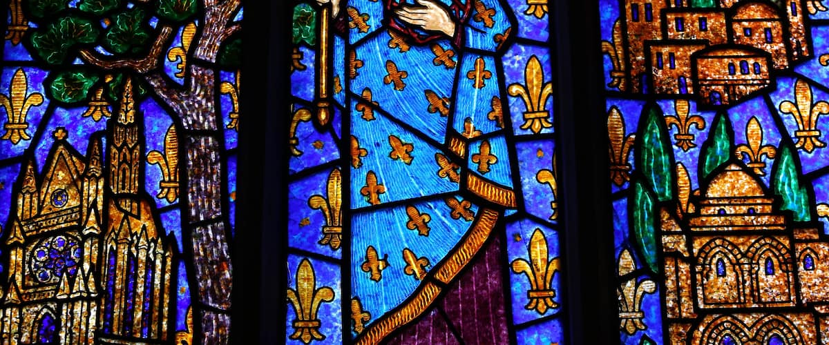 A stained glass window with a central figure holding a staff, surrounded by architectural elements and foliage.