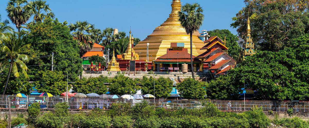 A golden pagoda surrounded by lush greenery and a river with boats.
