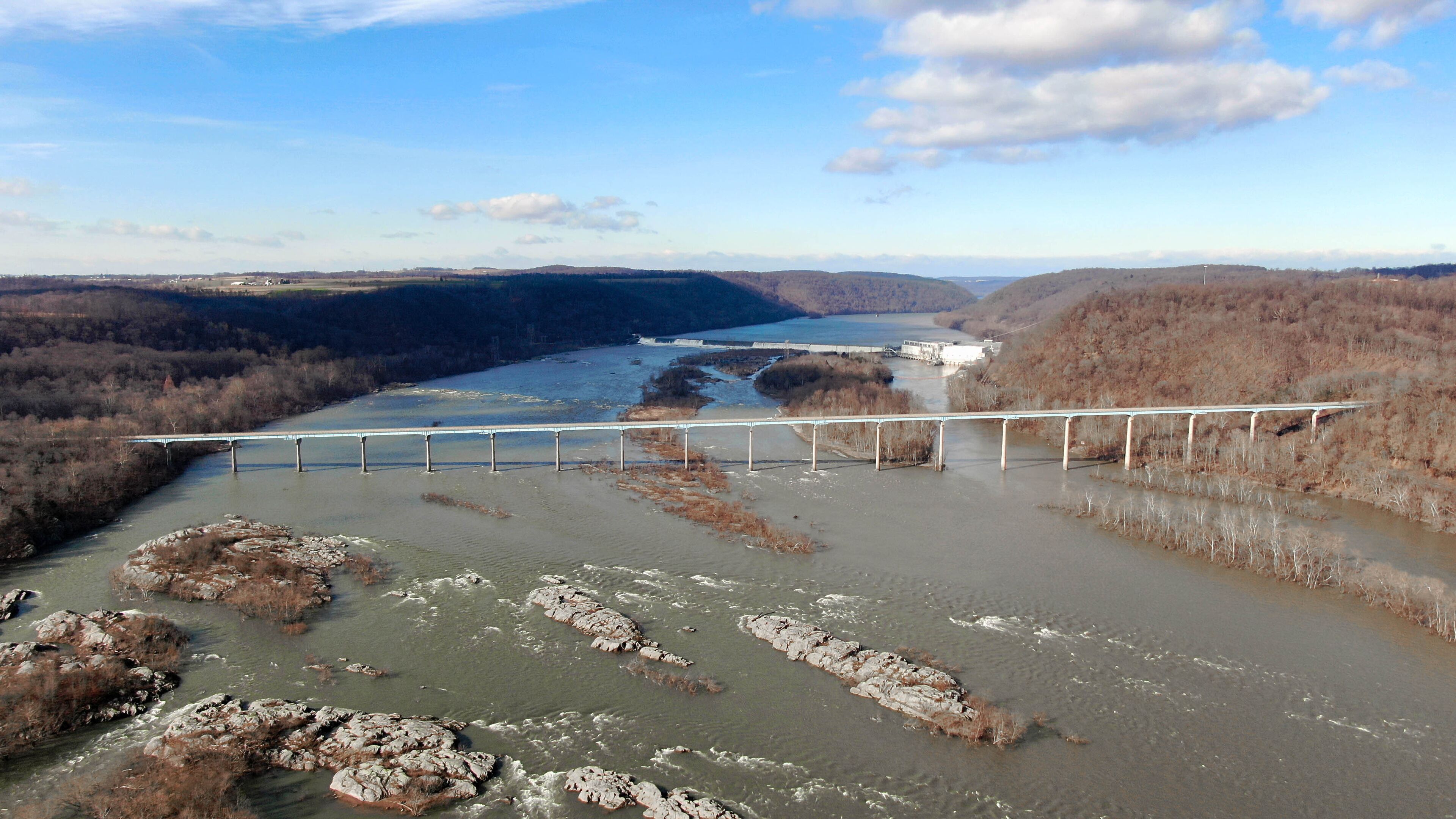 A river with a bridge spanning across it, surrounded by hills and sparse vegetation.