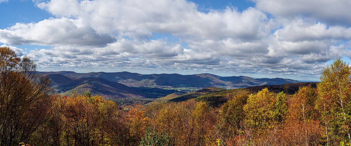 A mountainous landscape with autumn foliage and a partly cloudy sky.