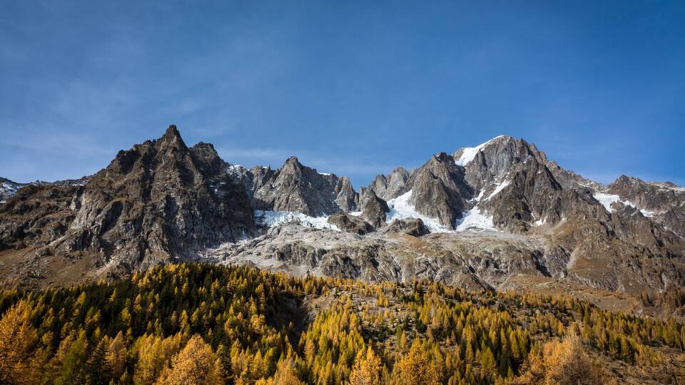 A mountain range with snow-capped peaks and a forested valley.