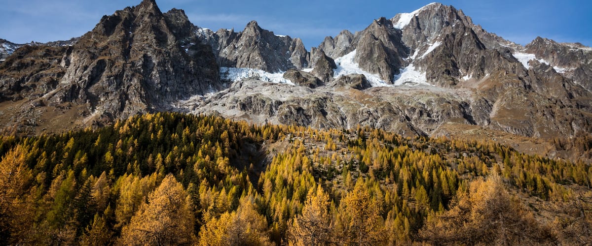 A mountain range with snow-capped peaks and a forested valley.
