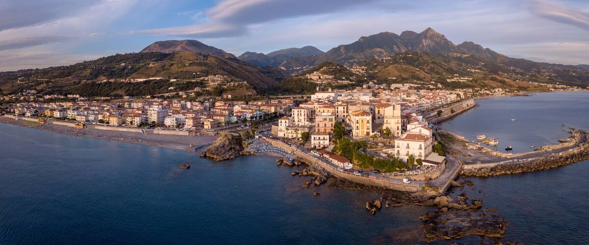 A coastal town with a prominent church, rocky coastline, and mountains in the background.