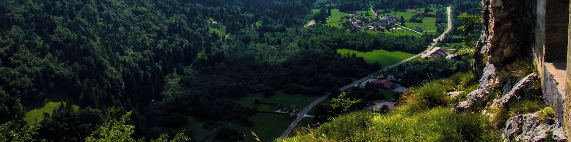 A mountainous landscape with a valley, a road, and a cliff.