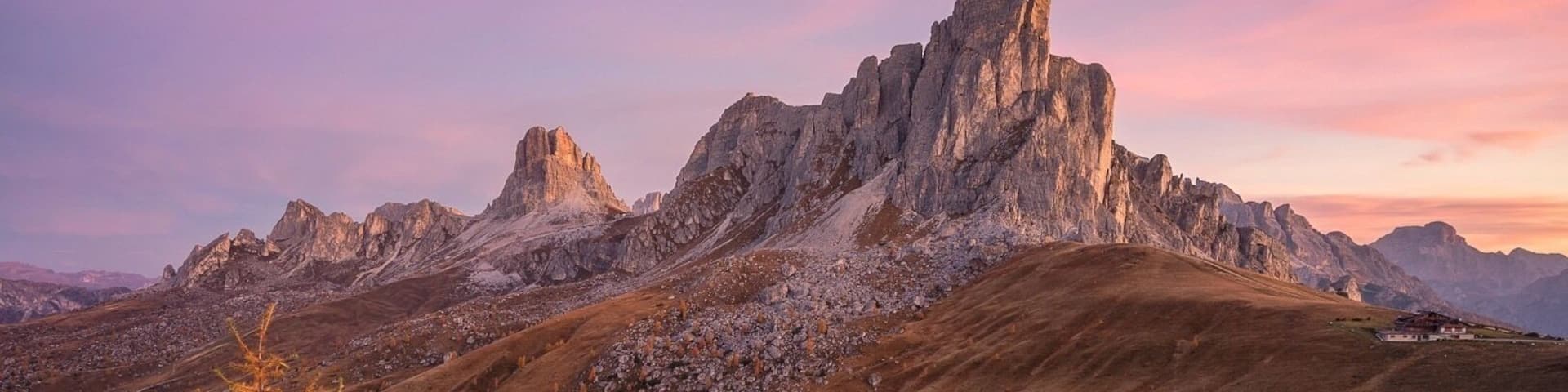 A mountainous landscape with a prominent rocky peak, winding roads, and sparse vegetation.