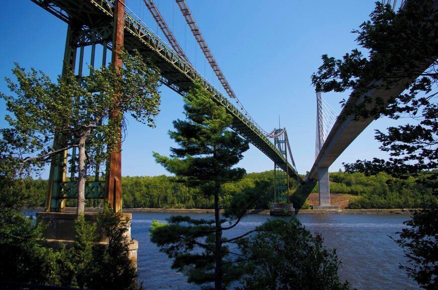 A large suspension bridge over a river, surrounded by trees and greenery.