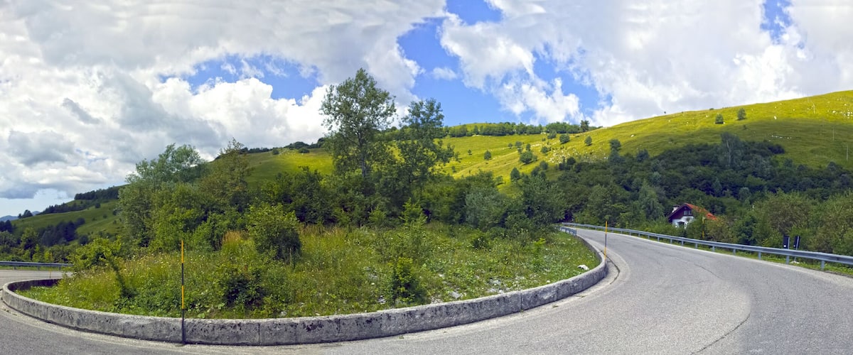 A winding road on a hillside with a view of the ocean and a clear sky.