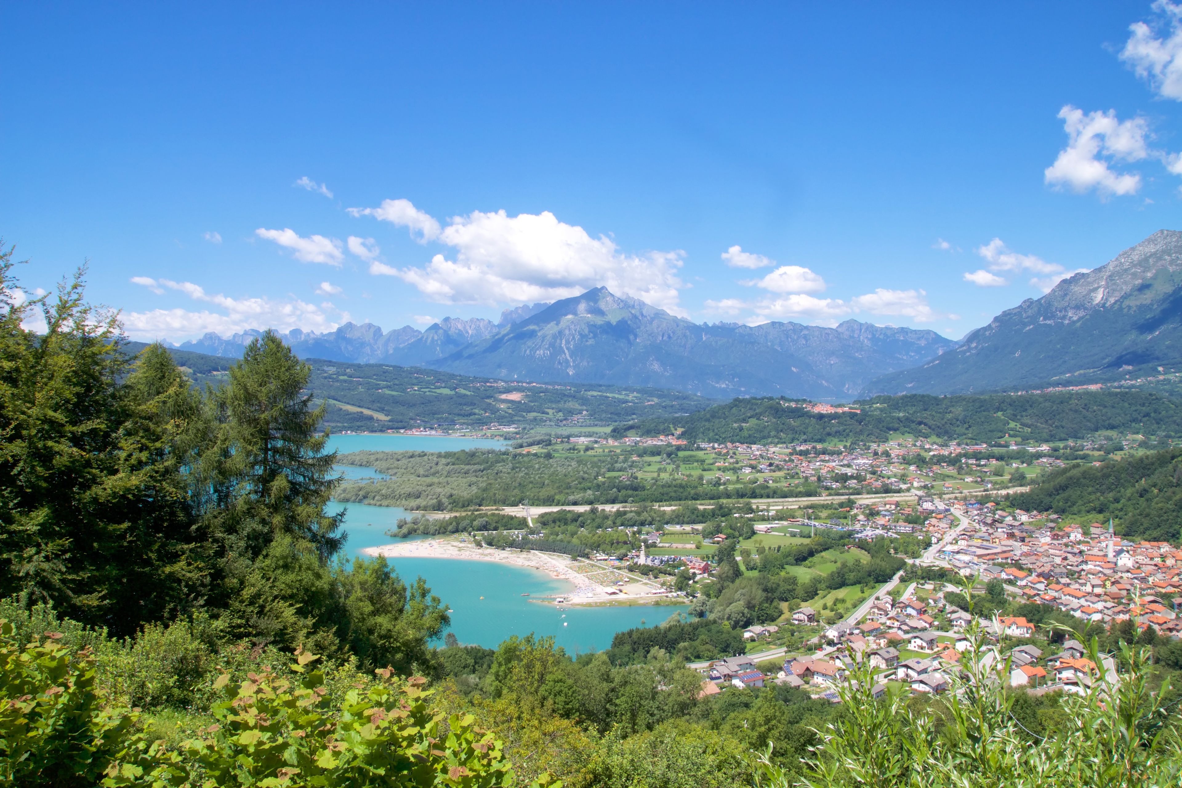 Un paysage montagneux avec une ville nichée au pied des montagnes, un lac et un ciel bleu azur.