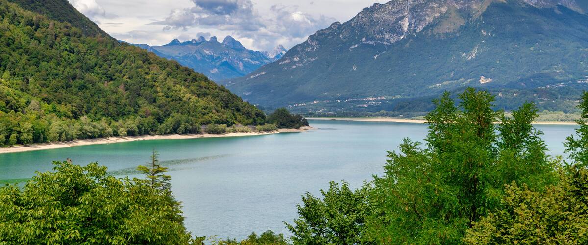 A lake surrounded by mountains, a beach, and dense green foliage.