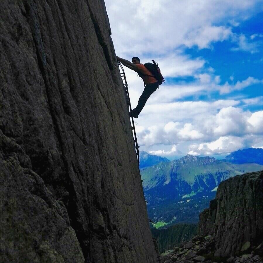 A person climbing a steep rock face with a mountainous landscape in the background.