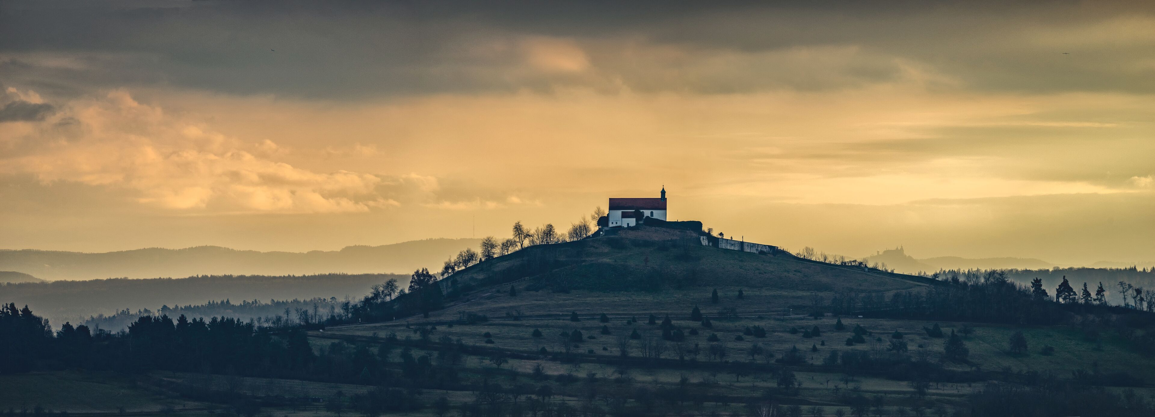 A solitary house on a hill with a cloudy sky.