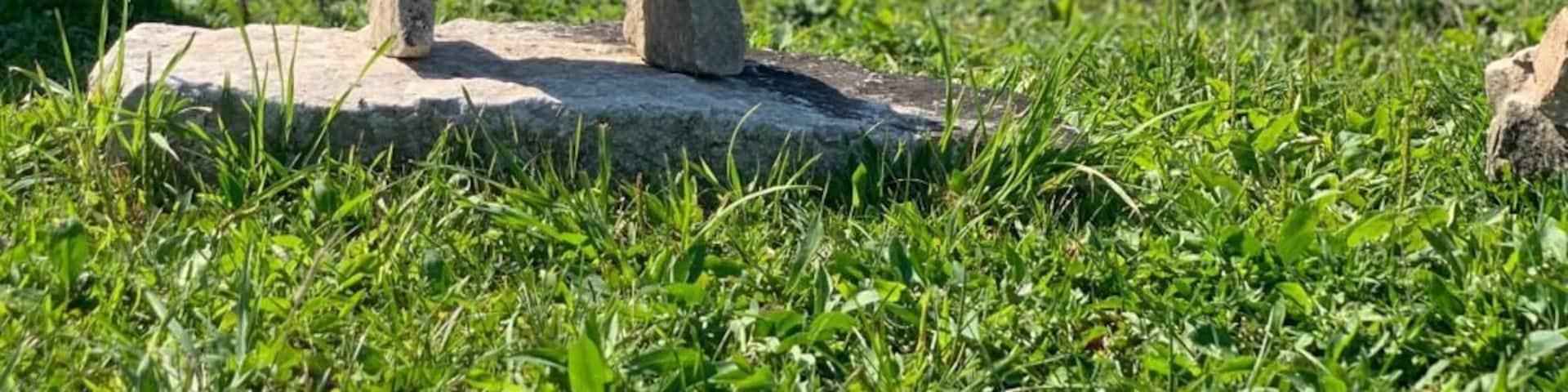 A stone structure in a grassy field with multiple stone stacks in the background.