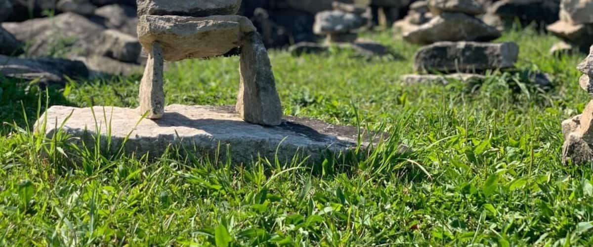 A stone structure in a grassy field with multiple stone stacks in the background.