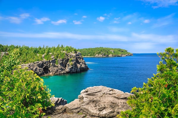 A coastal landscape with rocky outcrops, turquoise waters, and dense green foliage.