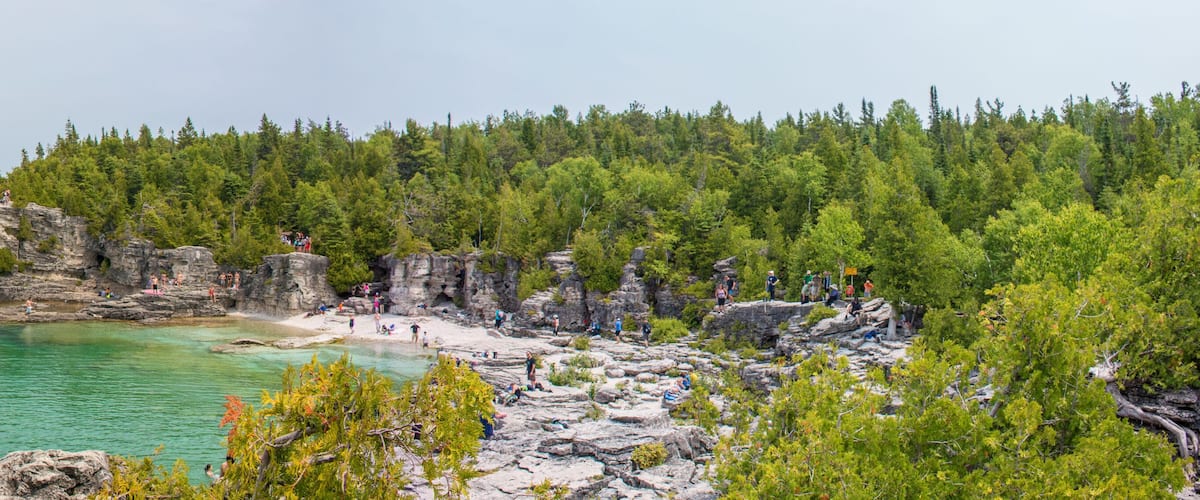 A rocky coastline with clear turquoise waters, dense green forest, and a small beach area.
