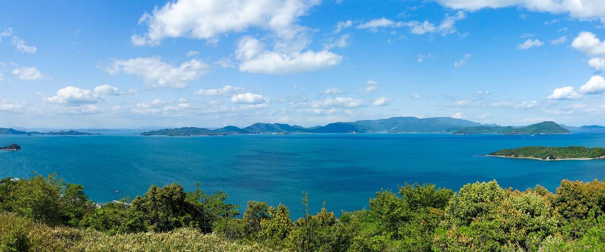 A coastal landscape with a clear blue sea, green hills, and scattered islands.