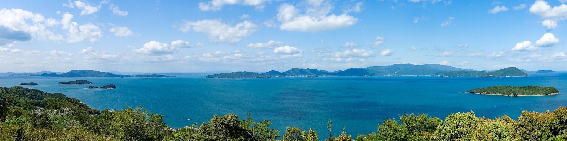 A coastal landscape with a clear blue sea, green hills, and scattered islands.