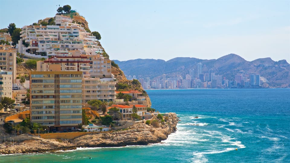 A coastal city with a prominent building on a cliff overlooking the sea, a rocky shoreline, and a distant city skyline.