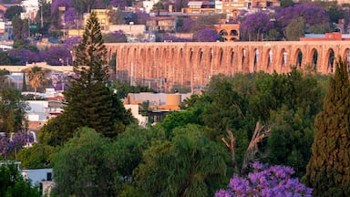 Un largo acueducto de piedra con arcos, rodeado de árboles y edificios.