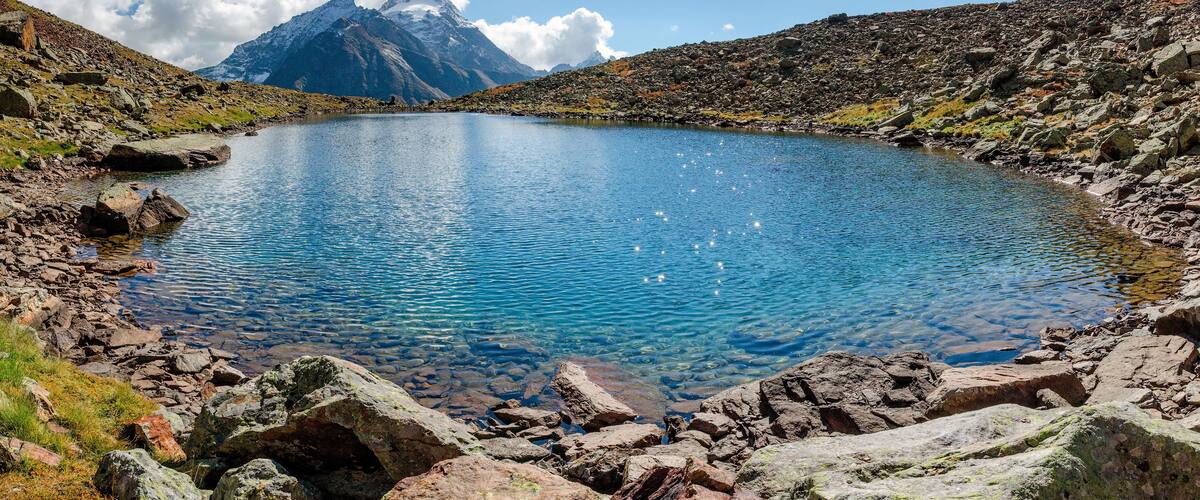 A clear mountain lake surrounded by rocky terrain and a prominent snow-capped peak in the background.