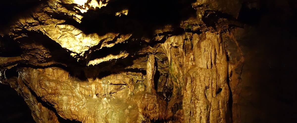 A cave with stalactites and stalagmites illuminated by artificial lighting.