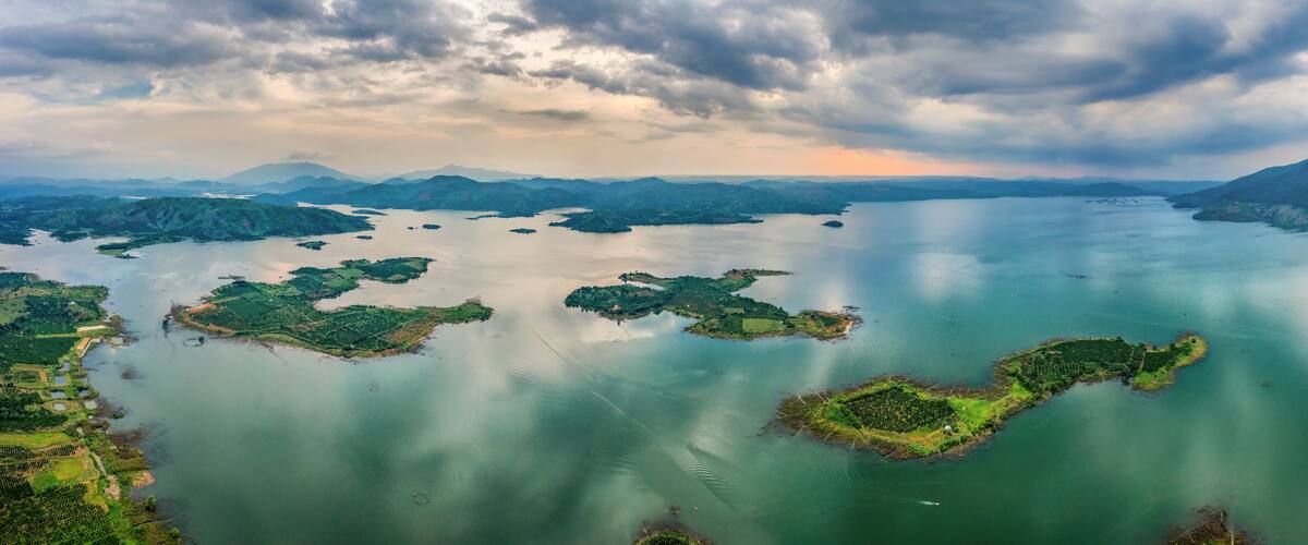 A vast lake surrounded by lush green islands and distant mountains under a cloudy sky.