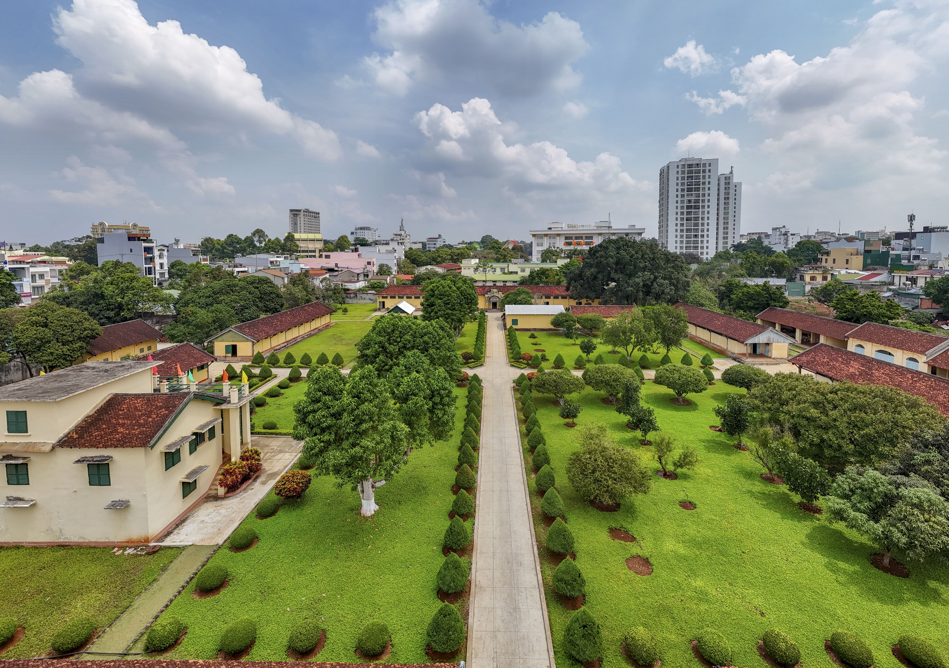Aerial view of the Dak Lak Museum with its red-tiled roofs contrasting against the vibrant green lawns and clear blue sky, Buon Ma Thuot, Dak Lak, Vietnam.