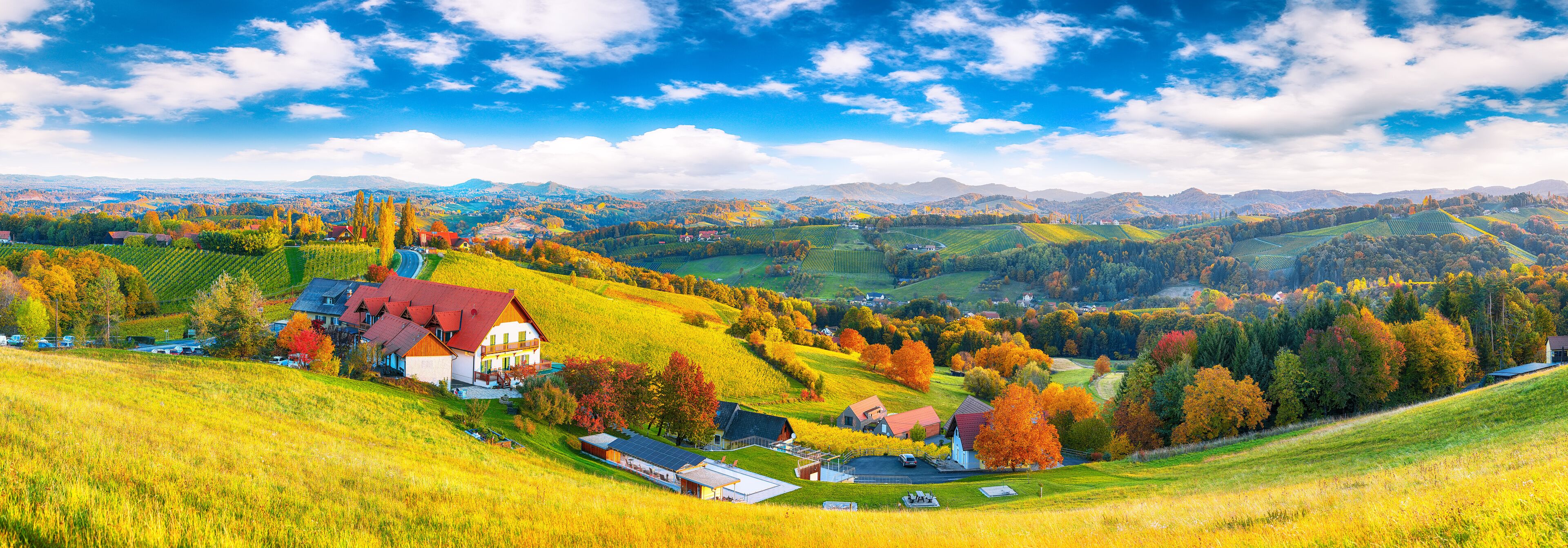 A rural landscape with rolling hills, a red-roofed house, and autumn-colored trees.