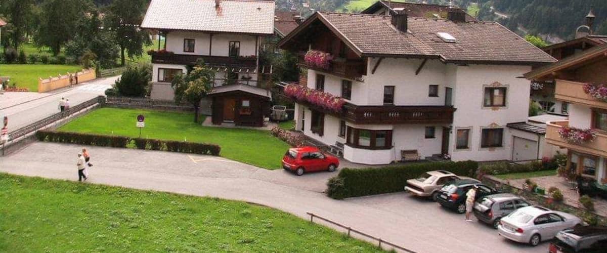 A mountainous village with traditional houses, a paved road, and parked cars.