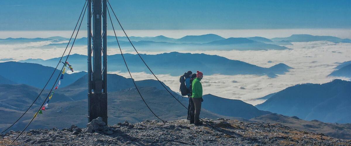 A cross on a mountain peak with hikers in the background.